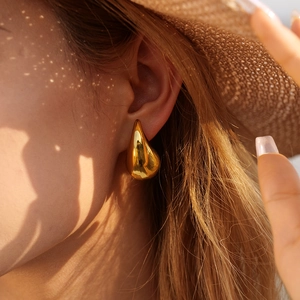 Close-up of a model wearing smooth golden teardrop earrings in natural sunlight