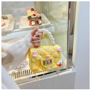 Close-up of yellow jelly bag with quilted pattern, pearl handle, and cute charms