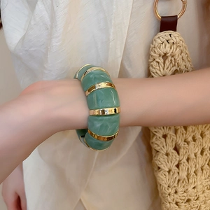 Detail of green marbled acrylic cuff bracelet with gold metal links on a model's wrist