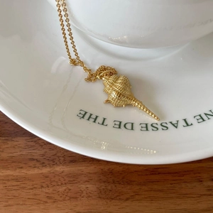 Detailed view of a golden conch shell pendant necklace on white ceramic and wooden surface