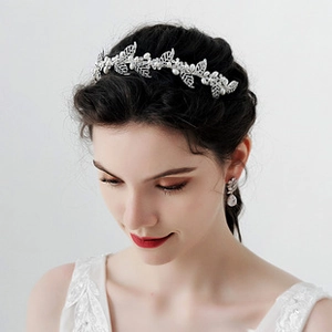 Detailed view of silver bridal hairband with leaf design, white pearls and teardrop earrings