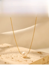 Macro detail of minimalist pearl pendant on a golden chain over textured stone backdrop