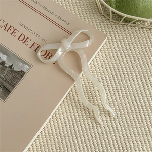 Close-up of white pearlescent bow U-shaped hair pin on a vintage book and woven mat