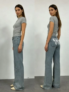 Dettaglio dei jeans a vita alta a gamba larga con stampa a farfalla bianca sulla tasca