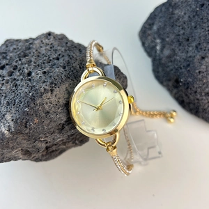 Detail of gold bracelet watch for women with diamond-encrusted bezel on dark rocks