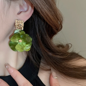 Detail shot of green acrylic flower earrings with textured gold metallic top pieces