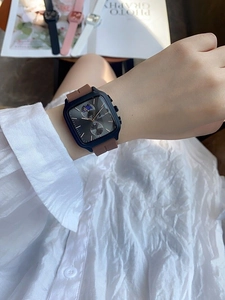 Close-up of a square dial watch with blue case and brown strap on a person's wrist