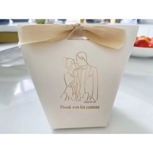 Close-up of a white wedding favor box with champagne ribbon and gold foil couple design