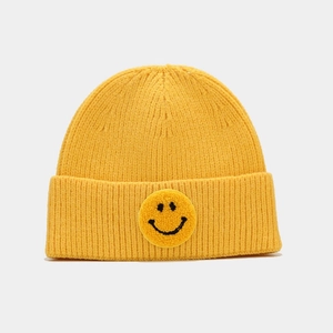 Détail d'un bonnet en tricot jaune avec un écusson de visage souriant noir