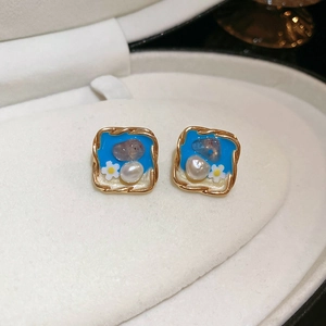 Vue macro de boucles d'oreilles carrées dorées avec insert bleu, perle et motif marguerite