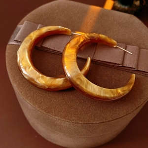Macro shot of amber resin C-shaped hoop earrings on a velvet brown jewelry box