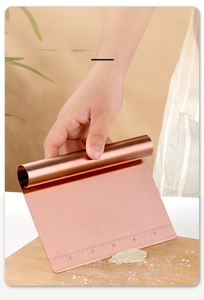 Rose gold stainless steel dough scraper with etched measurements used for cutting dough