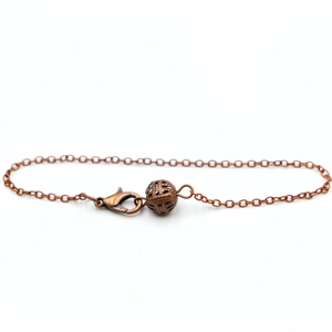 Detail of bronze metal pendulum chain featuring a hollow sphere charm and lobster clasp