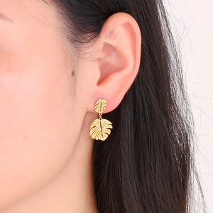 Detail showing gold monstera leaf earrings worn on ear with clear metallic texture