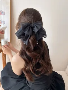Detail of a large black chiffon bow hair clip with elegant hanging bead droplets