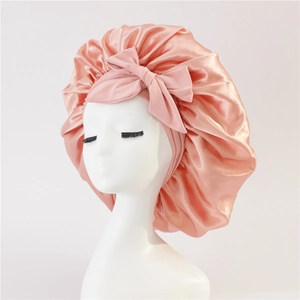 Detail of a pink satin silk sleep bonnet with a large decorative bow on a white mannequin