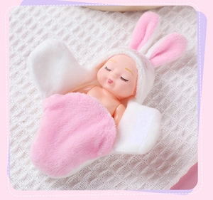 Close-up of a mini baby doll wearing a pink and white rabbit ear hooded sleep wrap toy