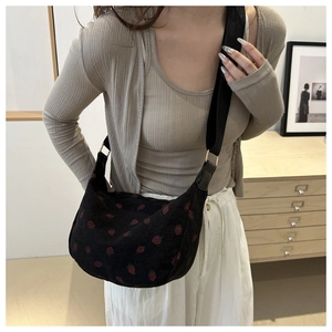 Detail of black corduroy shoulder bag featuring red strawberry print and nylon strap