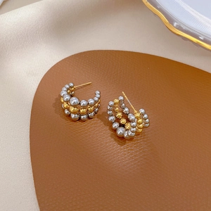 Close-up of two-tone gold and silver beaded C-hoop earrings on a soft satin surface