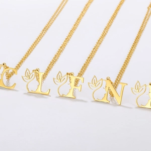 Detail of gold letter pendants featuring hollow silhouettes and leaf motifs on O-chains