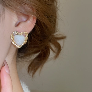 Close-up of elegant gold heart earring with pearlescent inlay worn by a model