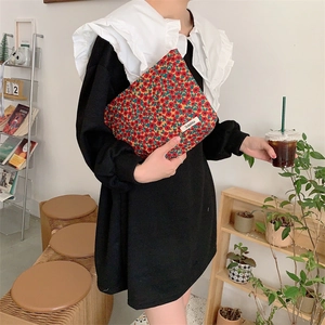 Détail d'une pochette en velours côtelé fleuri tenue par un mannequin dans un cadre cosy