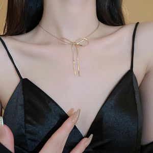Golden bow knot snake chain necklace with tassel detail shown on a model neck