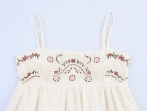 Detailed view of colorful floral embroidery and thin straps on a beige cotton dress