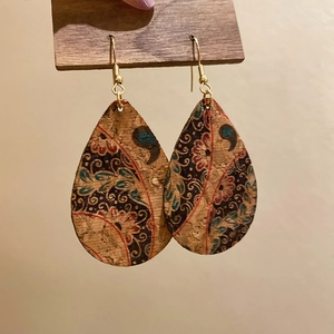 Detail of vintage teardrop leather earring with bohemian floral pattern on a wooden stand