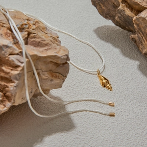Macro detail of a golden shell pendant on a white cord over textured rock background