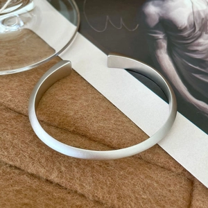 Detail of matte silver twisted cuff bracelet on brown suede with minimalist artistic backdrop