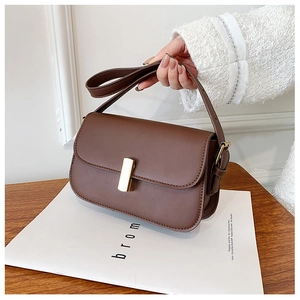 Close-up of brown vintage saddle bag with gold metal buckle on a wooden table