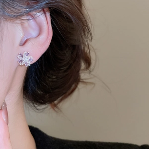 Close-up of elegant flower stud earrings with purple and white zircon stones on ear