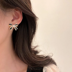 Elegant gold and black bow earrings with central pearl and diamonds on model