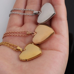 Hand holding three heart locket necklaces in silver, gold, and rose gold stainless steel