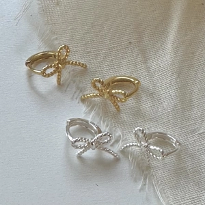 Detail of gold and silver bow earrings featuring a delicate woven texture on fabric