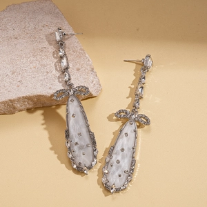 Détail de boucles d'oreilles nœud argenté avec gouttes opales et strass scintillants