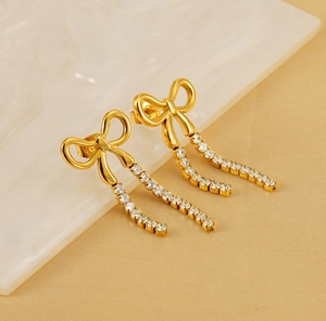 Close-up of golden bow earrings with sparkling rhinestone tassels on marble background