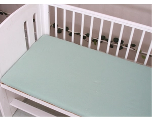 Close-up of soft mint green cotton fitted sheet on a white wooden baby crib