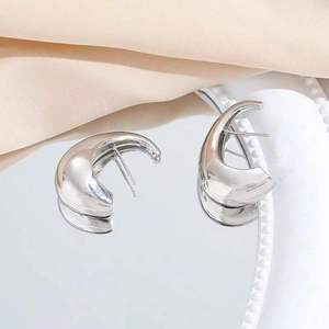 Modern polished silver crescent hoop earrings presented on a minimalist mirror surface