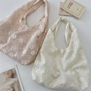 Close-up of floral embroidery on soft cream and pink fabric tote bags with a 3D texture