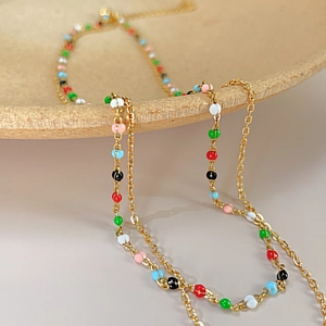 Vue macro du collier de perles colorées avec chaîne dorée sur céramique beige