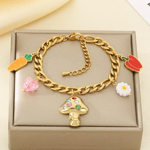 Detail of gold Cuban chain bracelet with mushroom, carrot and chili charms on silk fabric