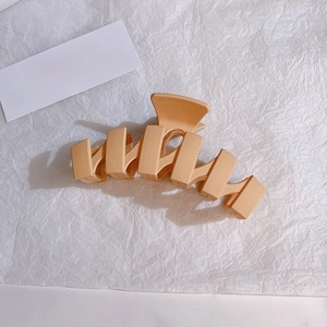 Macro view of large matte apricot hair claw clip on white textured paper background