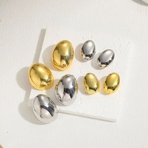 Polished oval hoop earrings in gold and silver finish on a minimalist textured block