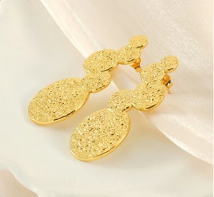 Detail of 18K gold-plated lava style earrings with irregular hammered texture on silk