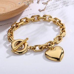 Polished gold curb chain bracelet featuring a heart pendant and toggle clasp on wood