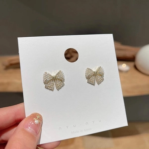 Detailed view of golden bow earrings featuring white faux pearls and cubic zirconia