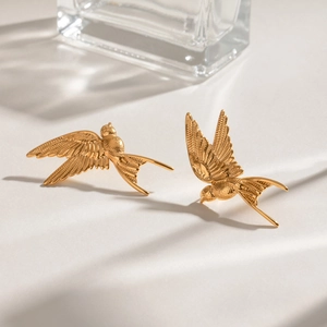 Macro detail of golden stainless steel bird earrings showing intricate feather textures