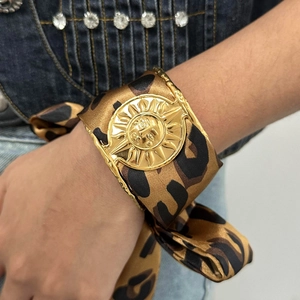 Exaggerated leopard silk wide cuff bracelet with a golden sun relief on blue denim background
